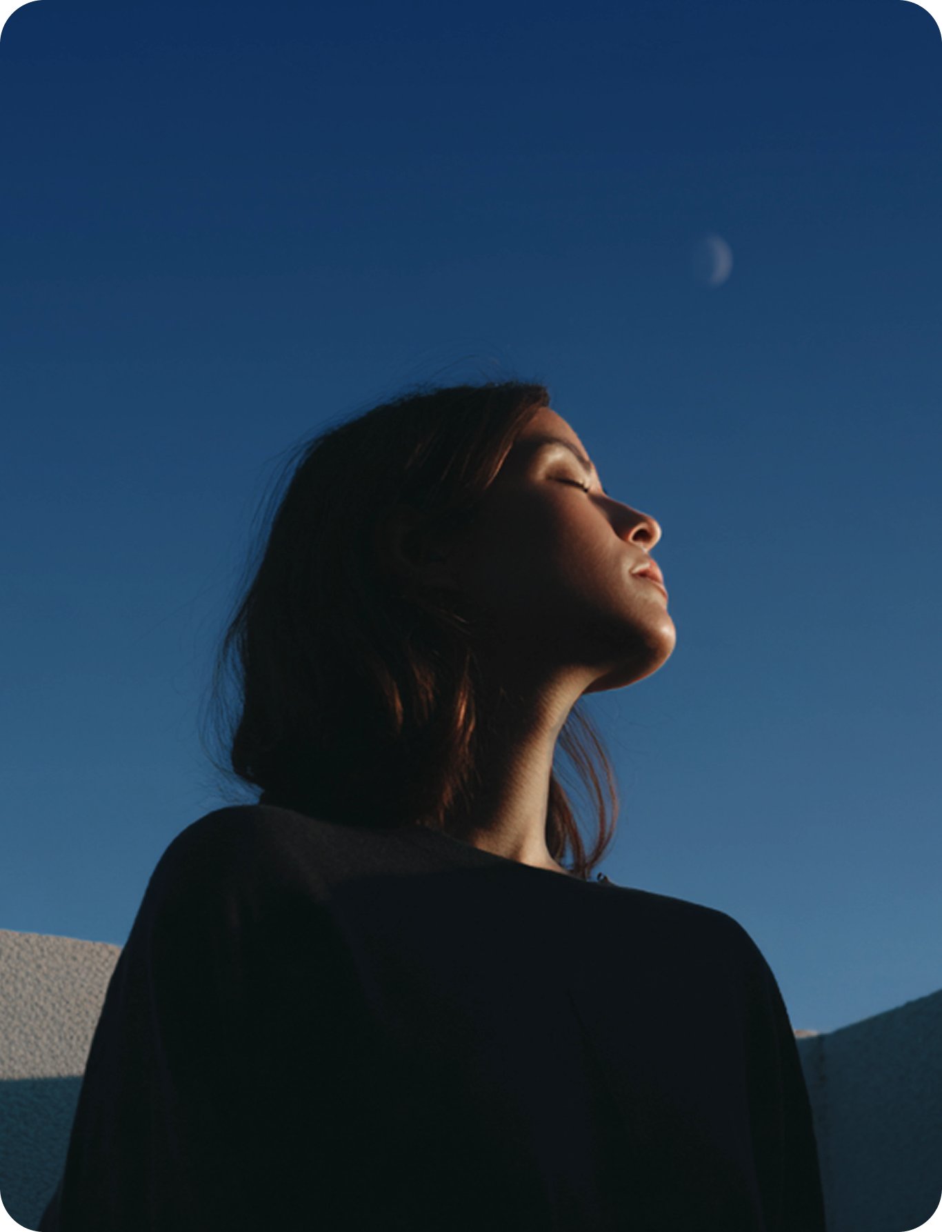 Person looking up toward a crescent moon in a twilight sky
