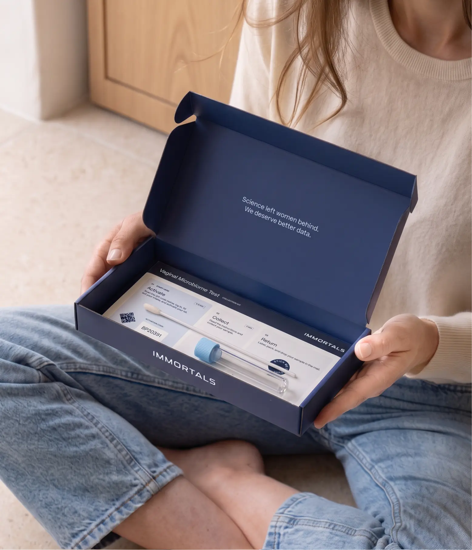 Woman sitting at home holding an open Immortals vaginal microbiome test kit